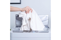 Image A hand placing a white shirt into a laundry machine.